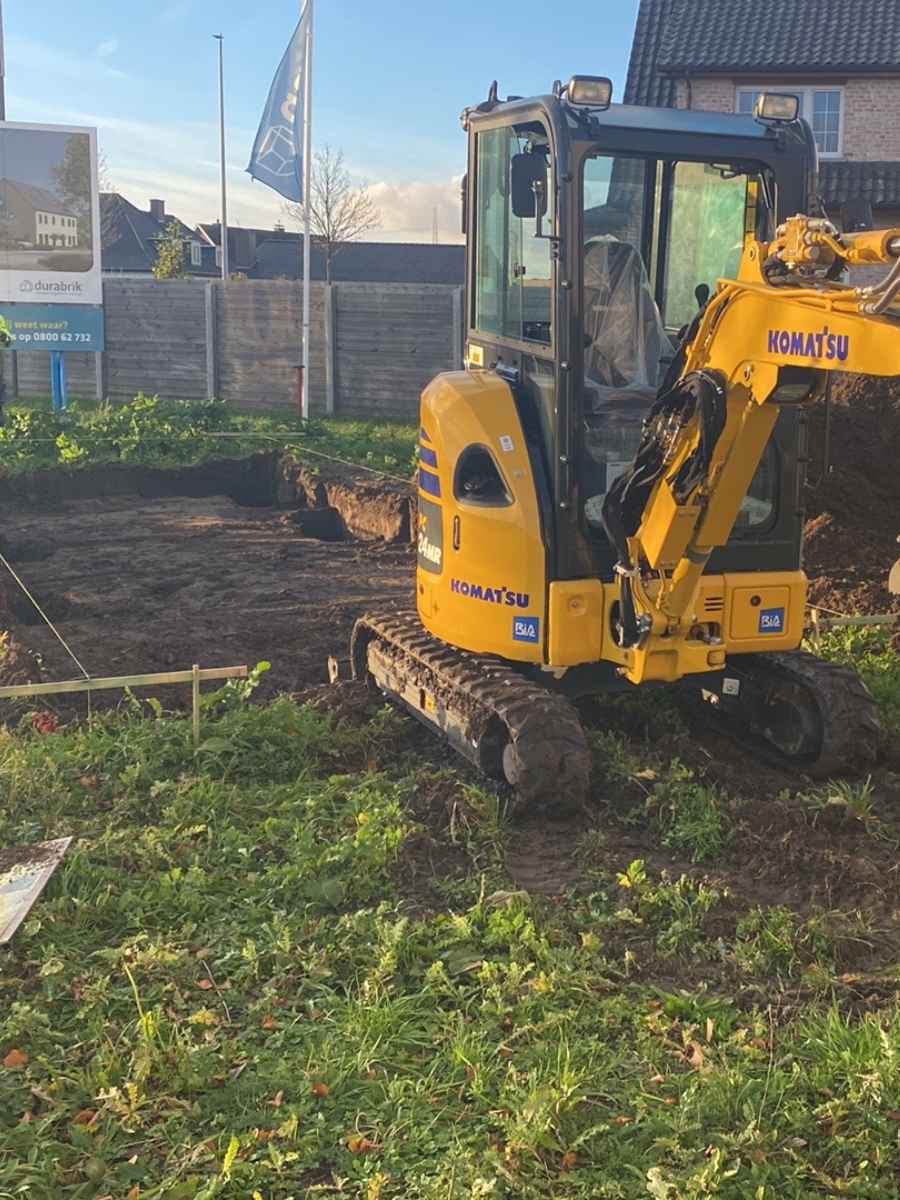 Graafmachine van JDC BV voert grondwerken uit ter voorbereiding van een tuinproject.